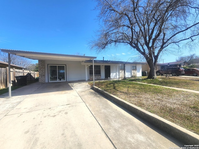 ranch-style home with fence, stone siding, driveway, a carport, and a front lawn