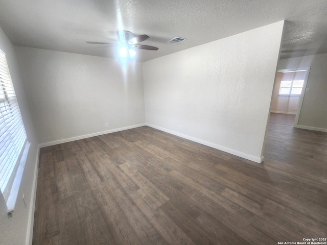 unfurnished room with baseboards, visible vents, a ceiling fan, dark wood-type flooring, and a textured ceiling