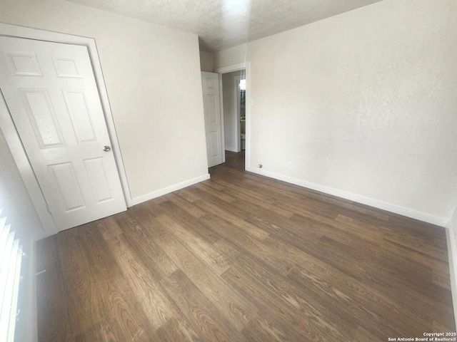 unfurnished room with baseboards, dark wood finished floors, and a textured ceiling