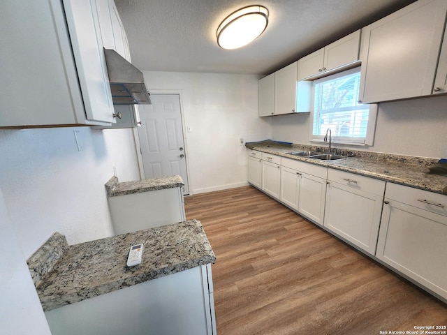 kitchen with light wood-style floors, a textured ceiling, white cabinetry, and a sink