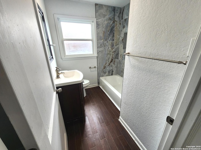 full bathroom featuring a textured wall, toilet, washtub / shower combination, wood tiled floor, and vanity