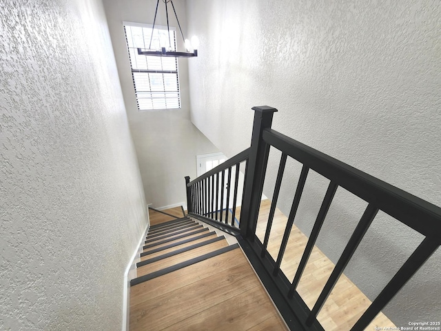 stairway with baseboards, wood finished floors, and a textured wall