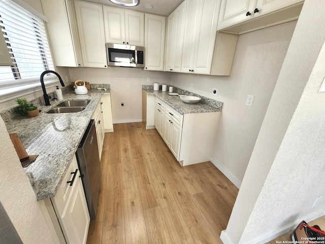 kitchen featuring light stone counters, light wood finished floors, stainless steel microwave, a sink, and baseboards