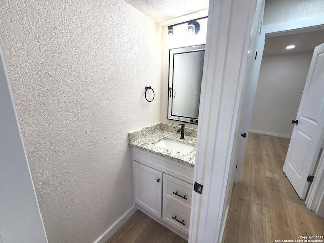 bathroom with vanity, baseboards, wood finished floors, and a textured wall