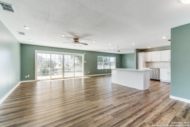 unfurnished living room with visible vents, a textured ceiling, baseboards, and wood finished floors