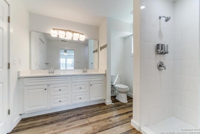 full bath with tiled shower, a sink, toilet, and wood finished floors