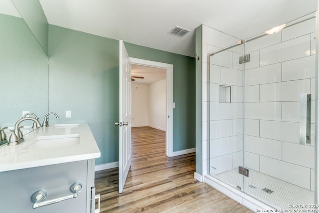 full bathroom featuring a sink, wood finished floors, a shower stall, and visible vents