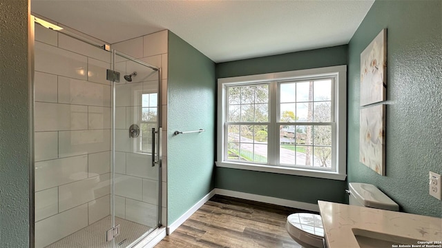 full bath with a textured wall, a stall shower, wood finished floors, and baseboards