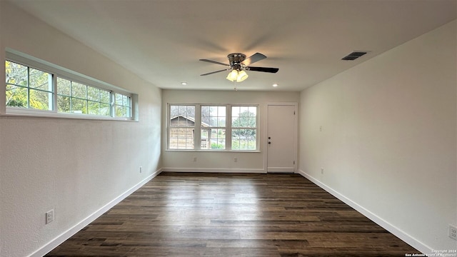 empty room with a wealth of natural light, dark wood finished floors, and visible vents