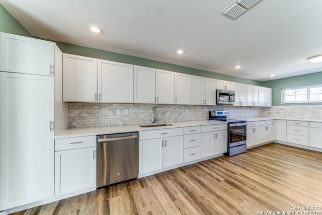 kitchen with visible vents, stainless steel appliances, light countertops, light wood-type flooring, and a sink