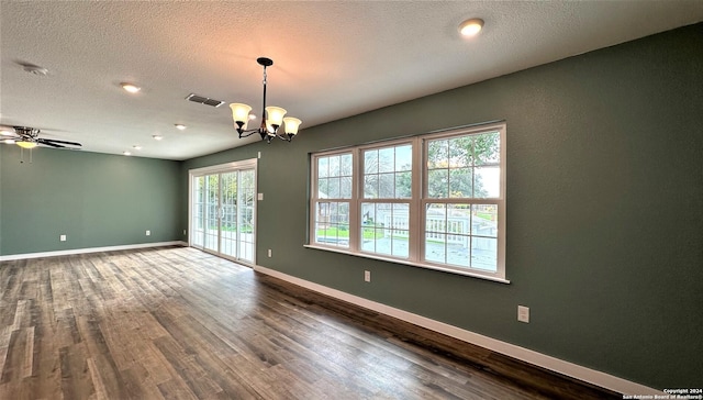 spare room featuring a textured ceiling, ceiling fan with notable chandelier, dark wood-style flooring, visible vents, and baseboards