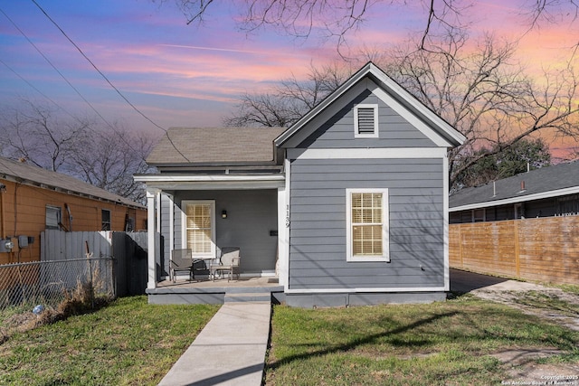 shotgun-style home featuring a front yard, covered porch, and fence