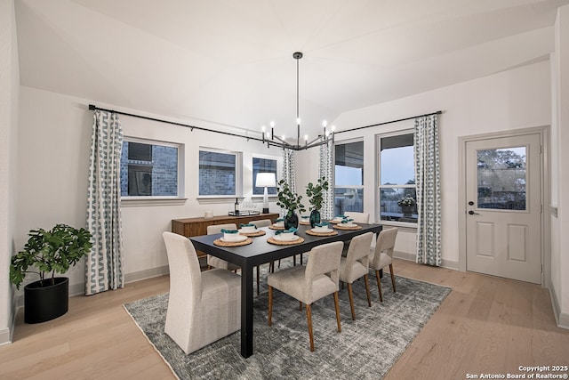 dining space featuring lofted ceiling, baseboards, light wood-style flooring, and an inviting chandelier