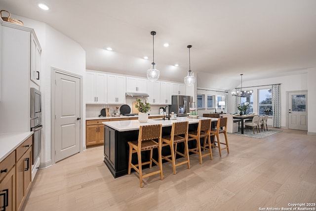 kitchen with a kitchen island with sink, a sink, light countertops, appliances with stainless steel finishes, and light wood finished floors