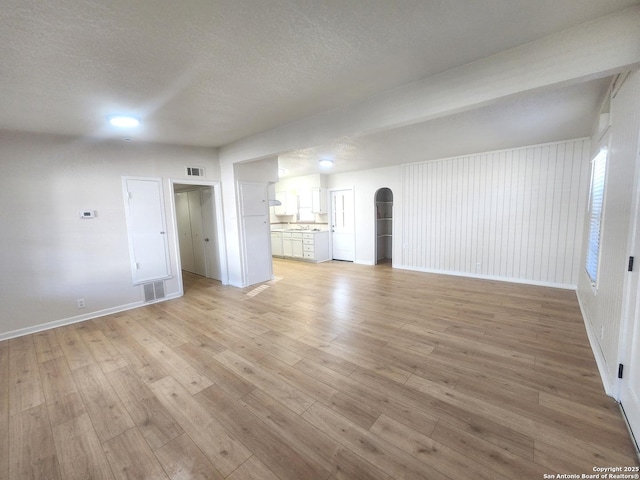 unfurnished living room with arched walkways, a textured ceiling, visible vents, baseboards, and light wood-style floors