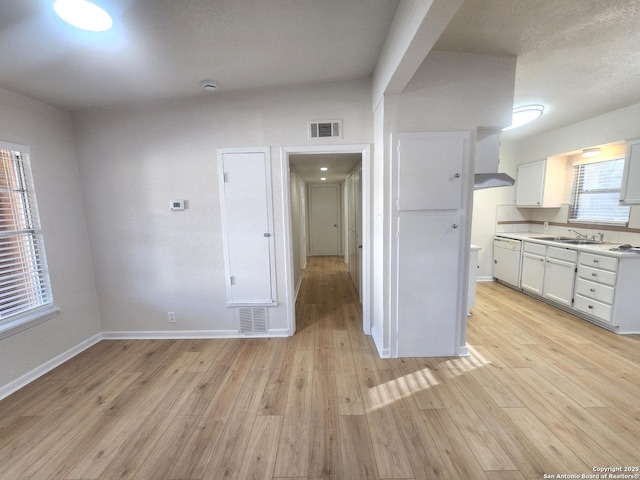 kitchen with visible vents, light countertops, light wood-style floors, white cabinetry, and a sink