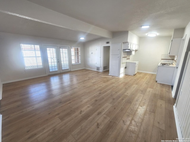 unfurnished living room featuring a textured ceiling, light wood-style flooring, visible vents, baseboards, and french doors