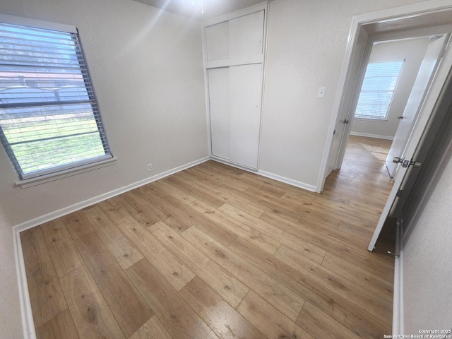 unfurnished bedroom featuring light wood-type flooring, a closet, multiple windows, and baseboards