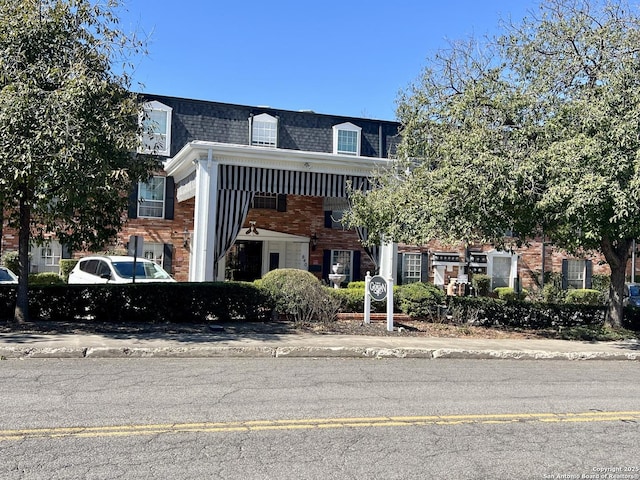 view of front of home featuring a shingled roof, mansard roof, and brick siding