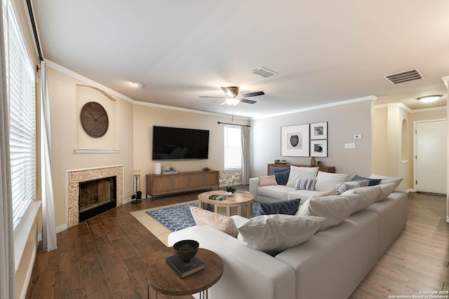 living area featuring a tiled fireplace, visible vents, arched walkways, and wood finished floors