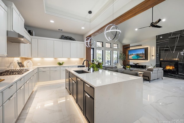 kitchen with stainless steel gas cooktop, a tiled fireplace, under cabinet range hood, marble finish floor, and a sink