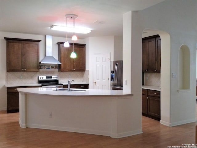 kitchen with light countertops, wall chimney range hood, appliances with stainless steel finishes, and dark brown cabinetry