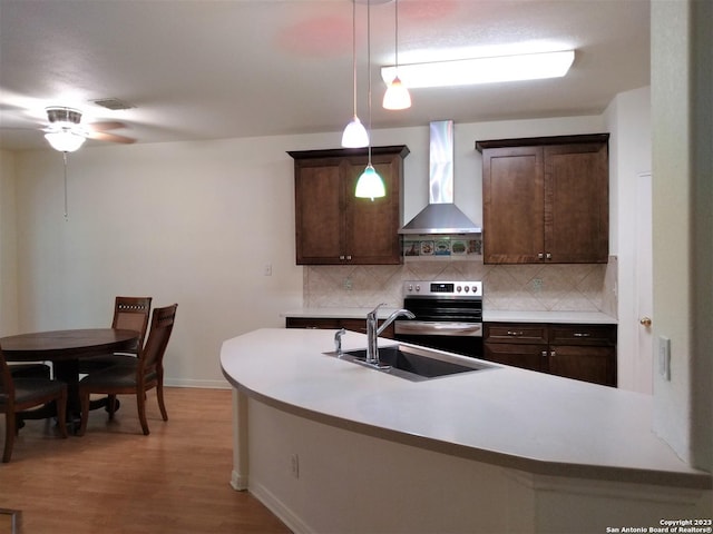 kitchen with wall chimney exhaust hood, backsplash, dark brown cabinetry, and stainless steel range with electric cooktop