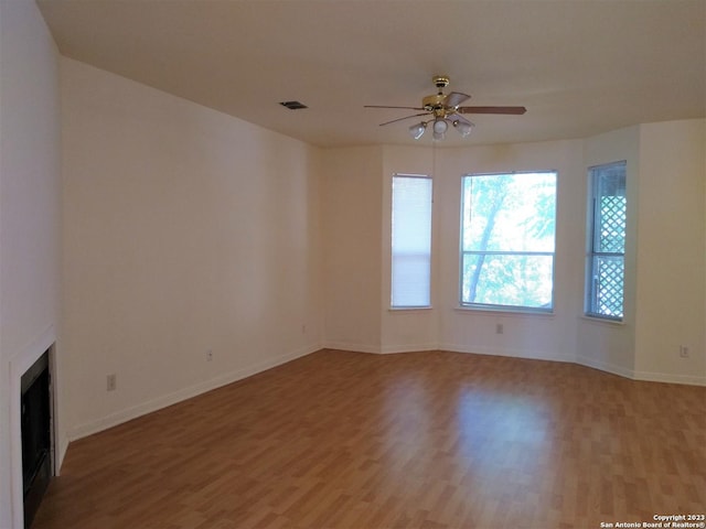 unfurnished living room featuring light wood finished floors, visible vents, baseboards, ceiling fan, and a fireplace