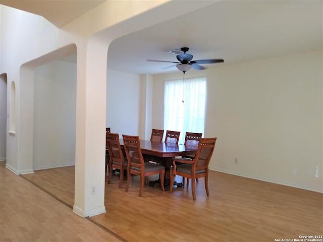 dining area featuring arched walkways, ceiling fan, light wood-type flooring, and baseboards