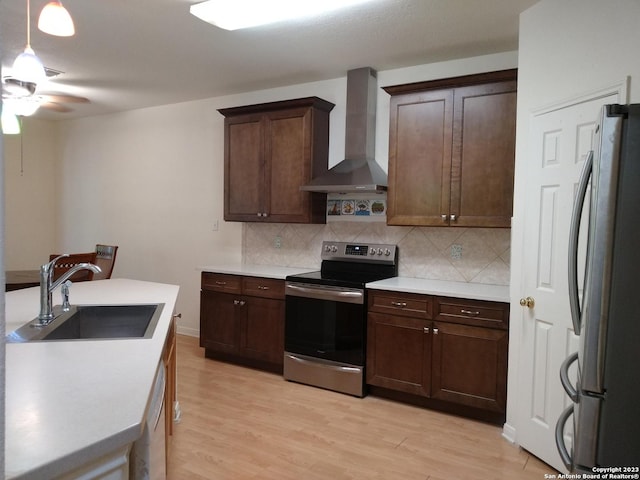 kitchen featuring stainless steel appliances, a sink, backsplash, and wall chimney exhaust hood