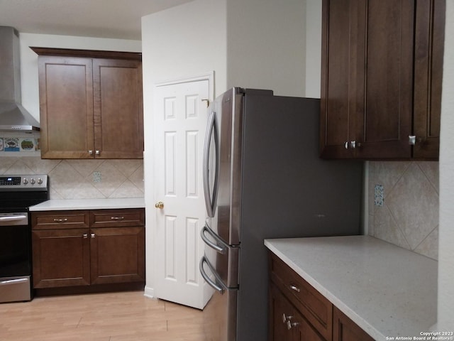 kitchen featuring tasteful backsplash, wall chimney exhaust hood, stainless steel appliances, and light wood-style flooring