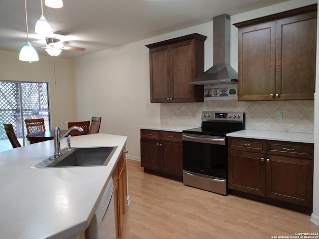 kitchen featuring light wood finished floors, dishwasher, stainless steel electric range, wall chimney range hood, and a sink