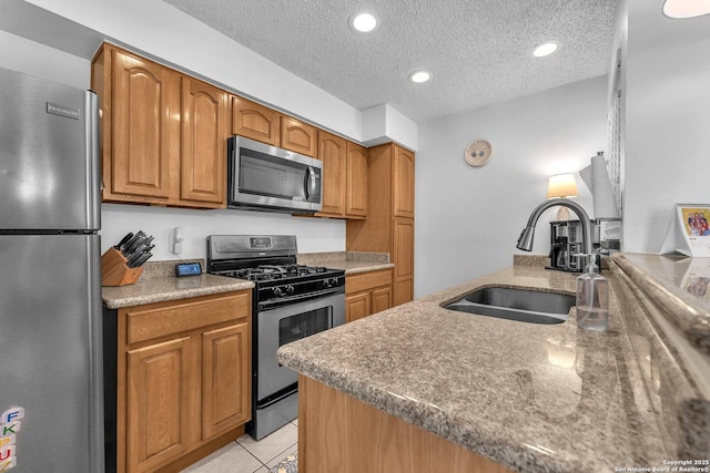 kitchen featuring brown cabinetry, stainless steel appliances, a textured ceiling, a sink, and light tile patterned flooring