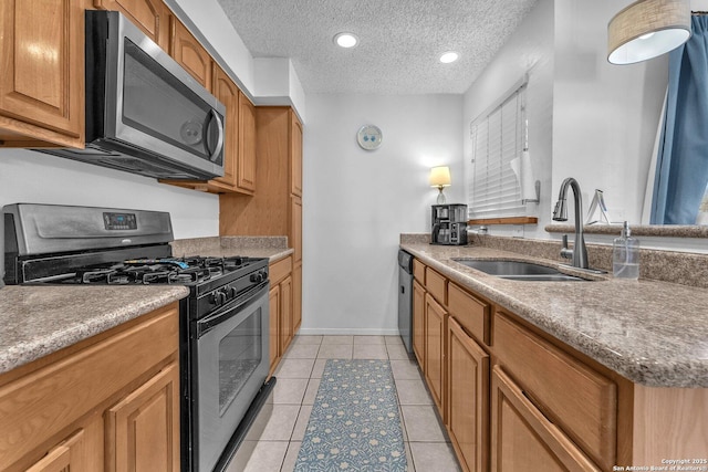 kitchen with light tile patterned floors, appliances with stainless steel finishes, a sink, a textured ceiling, and baseboards