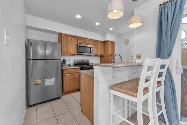 kitchen featuring light tile patterned floors, brown cabinetry, a breakfast bar area, stainless steel appliances, and a textured ceiling