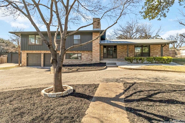 view of front of home featuring brick siding, driveway, an attached garage, and a chimney