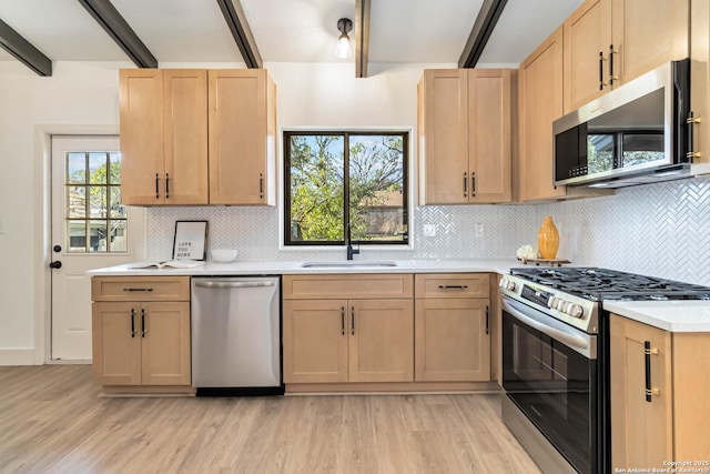 kitchen with beam ceiling, light brown cabinets, a sink, appliances with stainless steel finishes, and light countertops