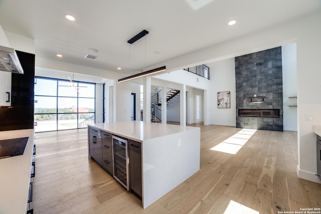 kitchen featuring a tiled fireplace, light wood-style floors, modern cabinets, beverage cooler, and stovetop