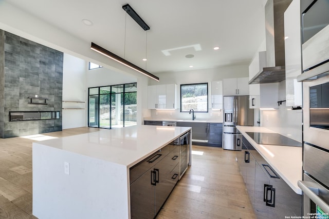 kitchen featuring wall chimney range hood, light wood-style flooring, modern cabinets, and stainless steel appliances