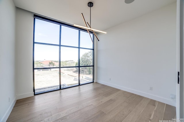 spare room featuring a chandelier, expansive windows, wood finished floors, and baseboards