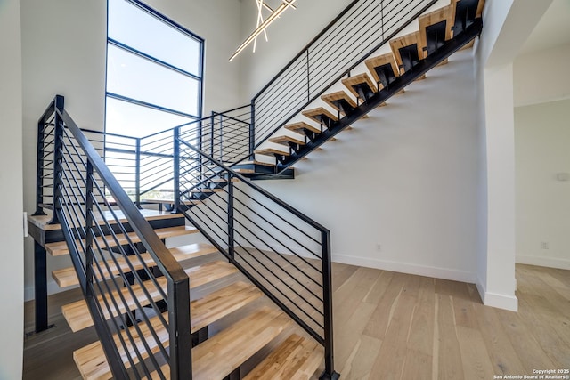 staircase featuring a towering ceiling, baseboards, and wood finished floors