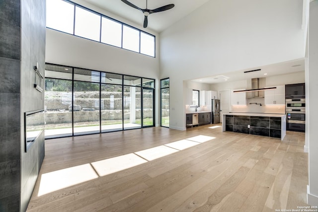 unfurnished living room with a ceiling fan, light wood-type flooring, and a sink