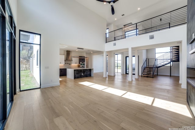 unfurnished living room with light wood finished floors, visible vents, stairway, a ceiling fan, and baseboards