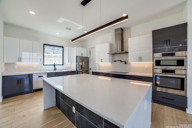 kitchen featuring stainless steel appliances, white cabinets, light countertops, light wood-type flooring, and wall chimney exhaust hood