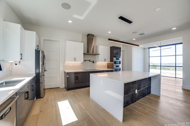 kitchen featuring visible vents, modern cabinets, stainless steel appliances, light wood-type flooring, and wall chimney range hood