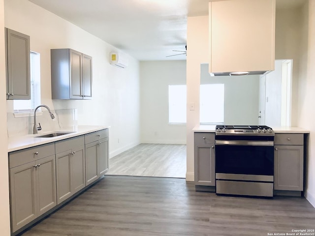 kitchen featuring stainless steel gas stove, a wall mounted AC, a sink, and gray cabinetry