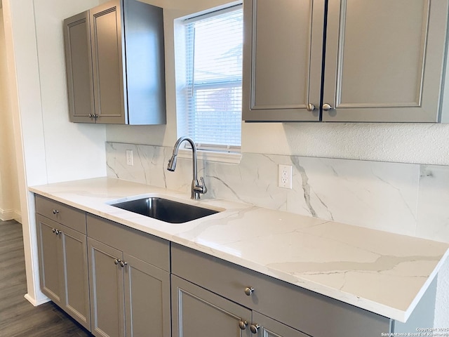 kitchen with light stone counters, gray cabinetry, a sink, tasteful backsplash, and dark wood finished floors