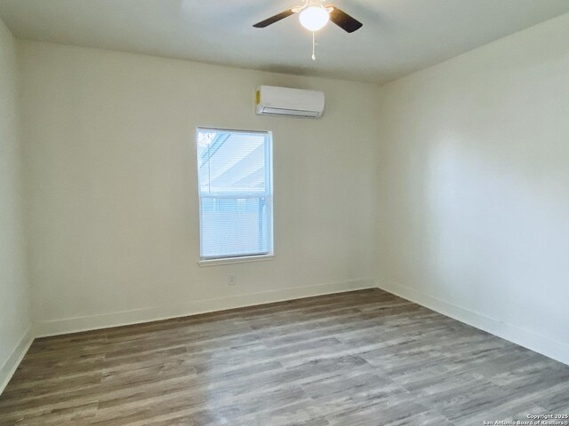 spare room with a wall unit AC, ceiling fan, baseboards, and wood finished floors