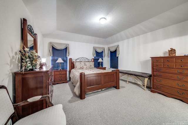 bedroom featuring light carpet, a tray ceiling, and a textured ceiling