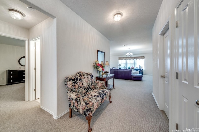 hall with carpet, a notable chandelier, a textured ceiling, and baseboards